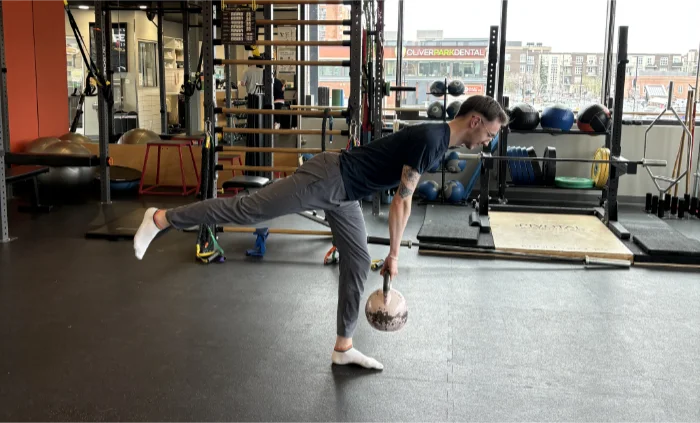 Individual performing Single Leg RDL by lifting one leg while holding a weight.